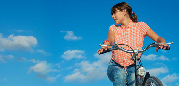 Low angle view of girl riding bicycle against blue sky