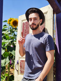 Portrait of young man holding camera while standing against wall