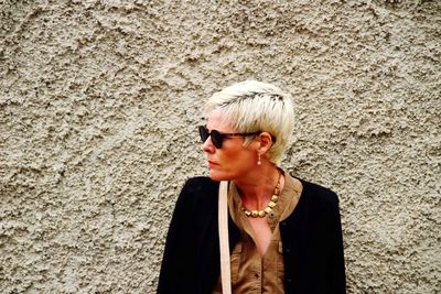 Mid adult woman wearing sunglasses standing against wall