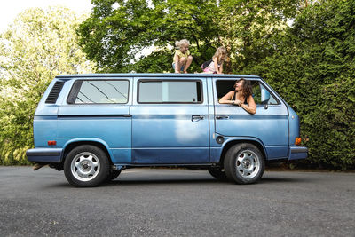 Mother and daughters laughing outside of vintage car window in summer