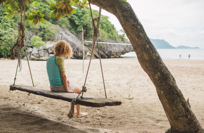 Full length of woman sitting on swing at beach