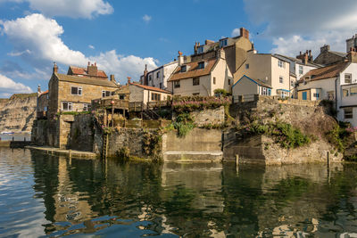 Buildings by river against sky in town