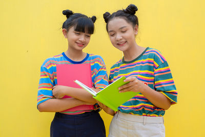 Portrait of a smiling girl standing against yellow wall