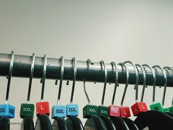 Close-up of various size labels on coathangers hanging from rack against white background