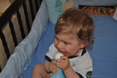 Cute boy playing with toy in crib at home