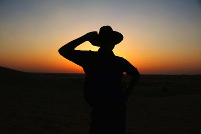 Silhouette man standing against orange sunset sky