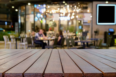 Empty wooden table against illuminated lights at restaurant