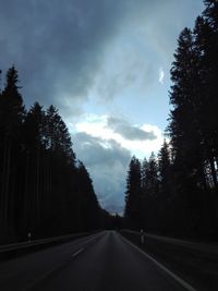 Empty road amidst trees in forest against sky