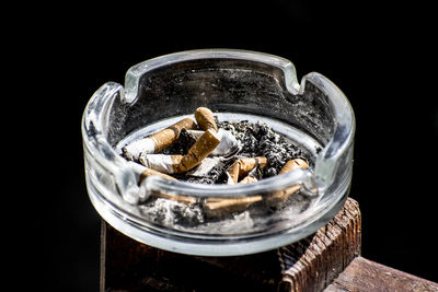 Close-up of cigarette butts in container against black background