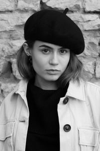 Portrait of young woman wearing hat standing against wall