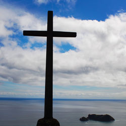 Cross on sea against sky