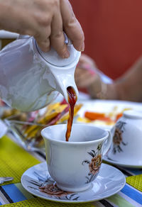 Midsection of person pouring coffee in cup on table