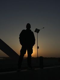 Low angle view of silhouette man standing by railing against sky during sunset