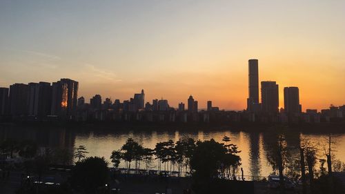 Silhouette of city at waterfront during sunset