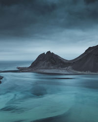 Scenic view of sea by mountains against cloudy sky