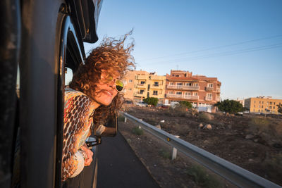 Woman peeking from car window against sky