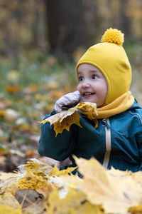 Cute girl holding autumn leaf sitting at park