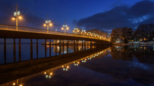 Illuminated bridge over river against sky at night