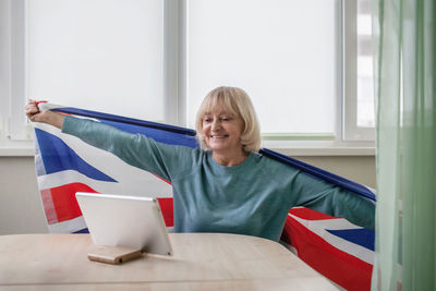 Smiling senior woman holding british flag at home