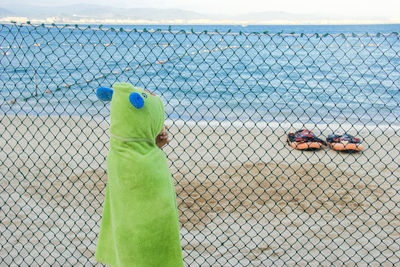 Girl wearing costume standing by chainlink fence against sea