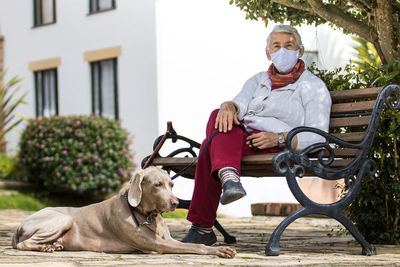 Full length of senior wearing mask with dog sitting outdoors