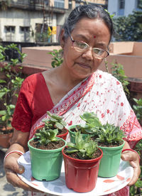 An aged woman holding a tray of miniature succulents and other decorative garden plants in pots.