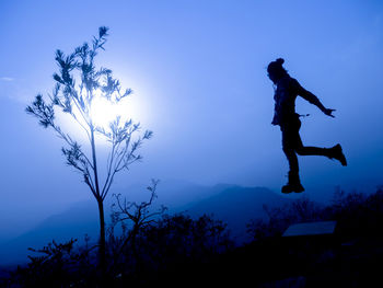 Low angle view of silhouette man against trees against blue sky