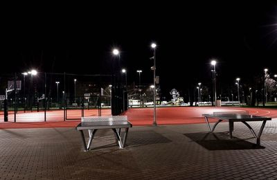 Empty benches against illuminated city at night
