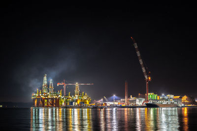 Illuminated commercial dock by sea against sky at night