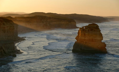 Rock formation on sea against sky during sunrise