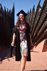 Portrait of smiling young woman standing against building in graduation robes