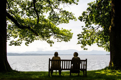 Rear view of people sitting on bench at lakeshore