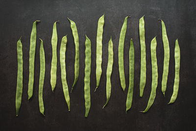 Top view of whole green beans in a row on dark background