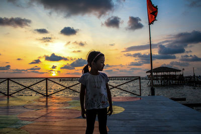 Woman standing on pier over sea against sky during sunset
