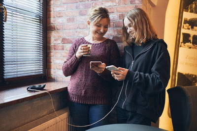 Smiling women using smartphones drinking coffee charging mobile phone relaxing in office