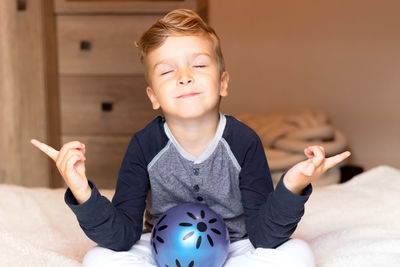 Small boy practicing yoga and meditating with eyes closed on a bed.