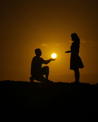 Silhouette couple against orange sunset sky