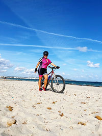 Low section of man riding bicycle on beach against sky