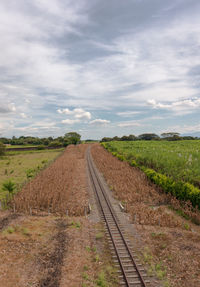 Empty railroad track amidst field against sky