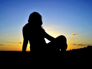 Silhouette people sitting on beach against sky during sunset