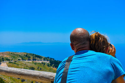 Rear view of man and daughter against blue sky