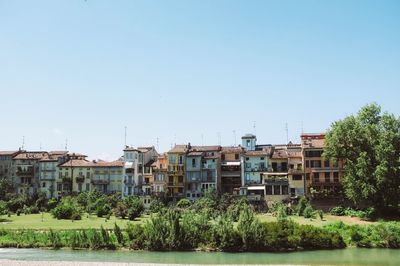 Houses by river and buildings against clear sky