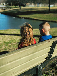 Rear view of girl and boy sitting on bench at park