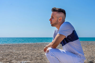 Man wearing sunglasses on beach against blue sky