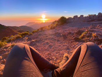 Low section of woman relaxing on mountain against sky during sunset