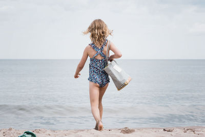 Young girl holding a beach bag strutting towards the sea