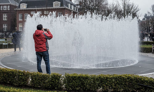 Man photographing fountain by house