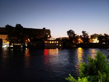 River by illuminated buildings against clear sky at night