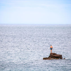 Mid distance of shirtless man standing on rock in sea against sky