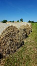 Hay bales on field against clear blue sky